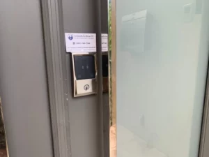 A smart access control keypad and lock system installed on a metal frame door, with a Locksmith For Bronx NY business card placed above.